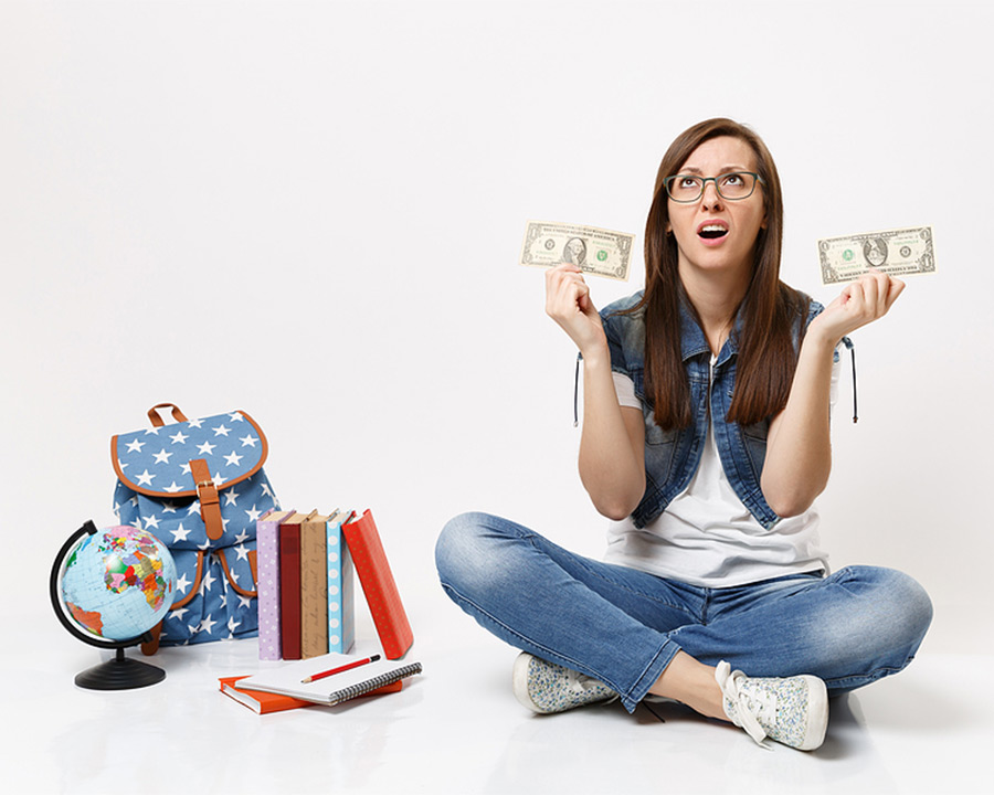young woman in blue jeans sitting next to a small globe with stack of books and book back nearby
