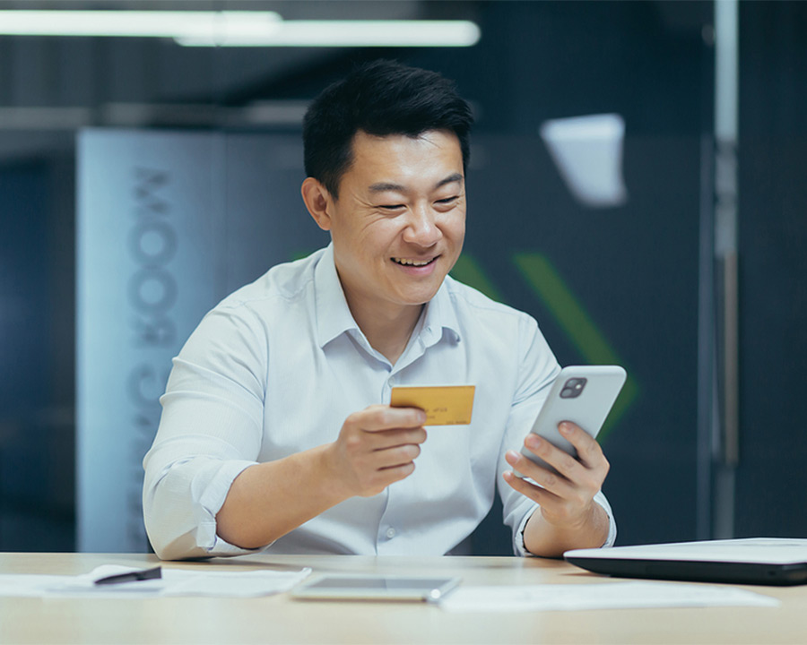 man holding a debit card while shopping on his mobile phone