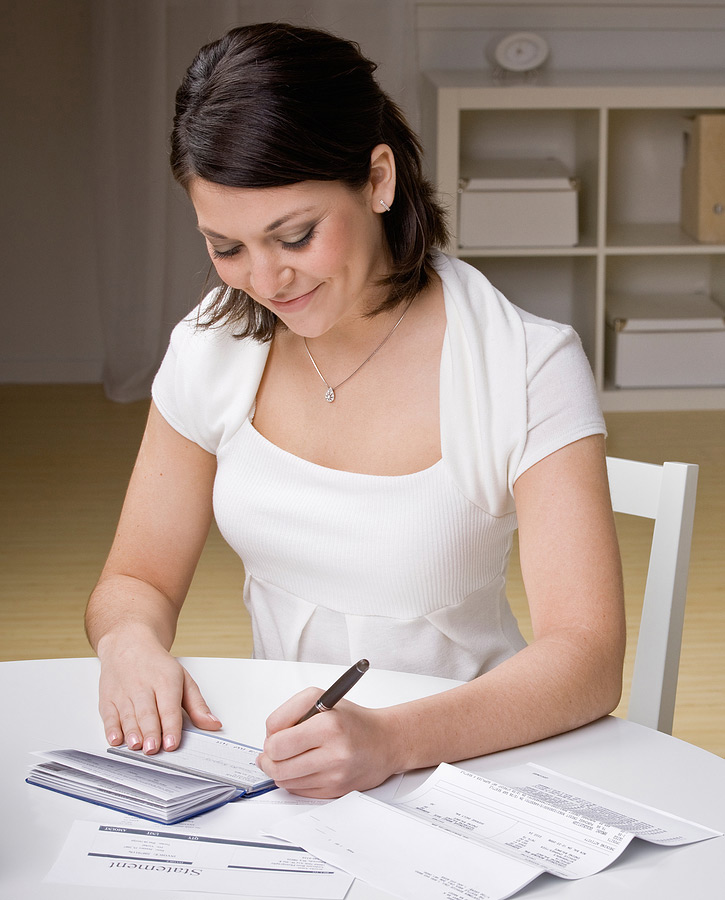 woman sitting at table writing a check to pay a bill