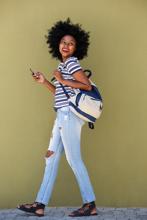 young woman carrying a backpack while checking her text messages