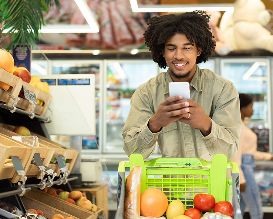 man shopping for groceries while checking his account balance via text message