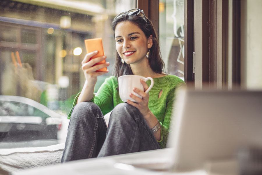 Smiling woman looking at cell phone and holding coffee cup